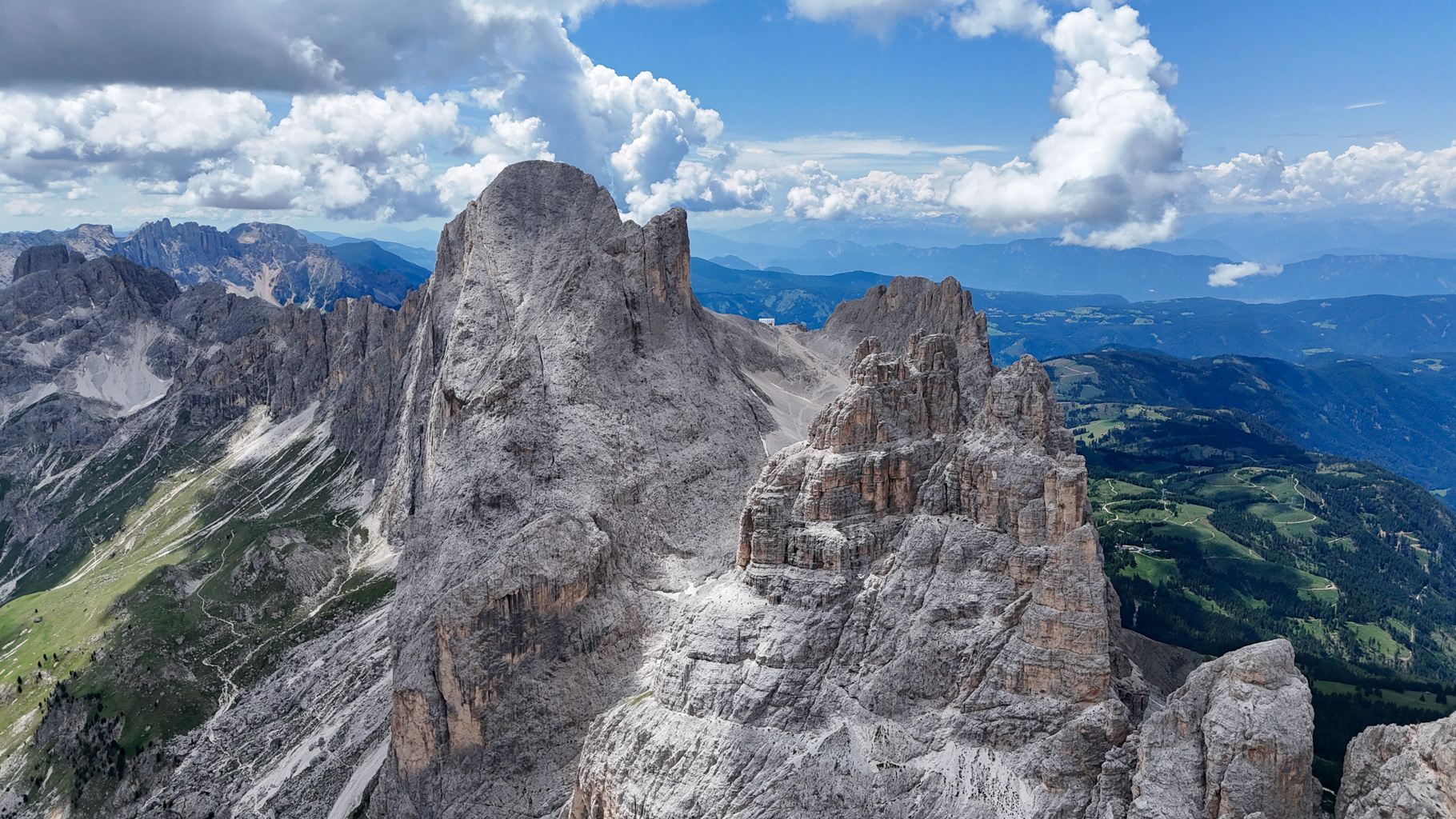 Letecký pohľad na veže Vajolet, ikonickú dominantu Dolomitov. V pozadí vidno aj horskú chatu Rifugio Passo Santner pod vrcholom Rosengartenspitze, ktorá je obľúbeným cieľom horolezcov.