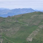 Foto 6: Pohľad cez údolie na rozľahlé trávnaté hrebene Secedy s chatami a lanovkami, v diaľke sa vrstvia ďalšie pohoria.