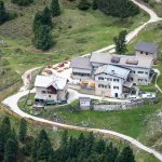 Foto 9: Pohľad zhora na rozsiahlu chatu Rifugio Firenze (Regensburger Hütte) so slnečnou terasou, obklopenú lúkami a chodníkmi.