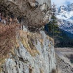 Foto 6: Spodná časť via ferraty - ľudia kráčajúci po chodníku nad jazerom, pričom ferrata vedie popod nimi