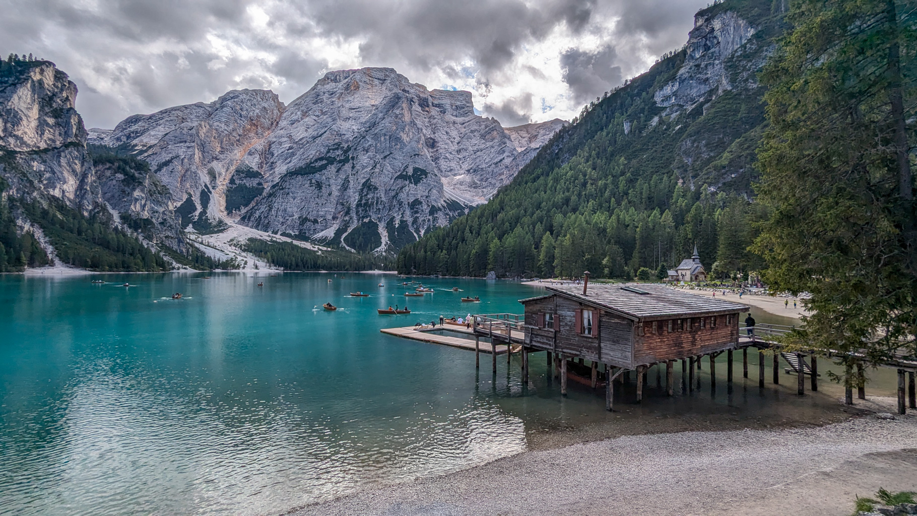 Lago di Braies v obklopení strmých stien Dolomitov s ikonickým dreveným mólom a požičovňou člnov. V pozadí dominuje vrch Croda del Becco (Seekofel).