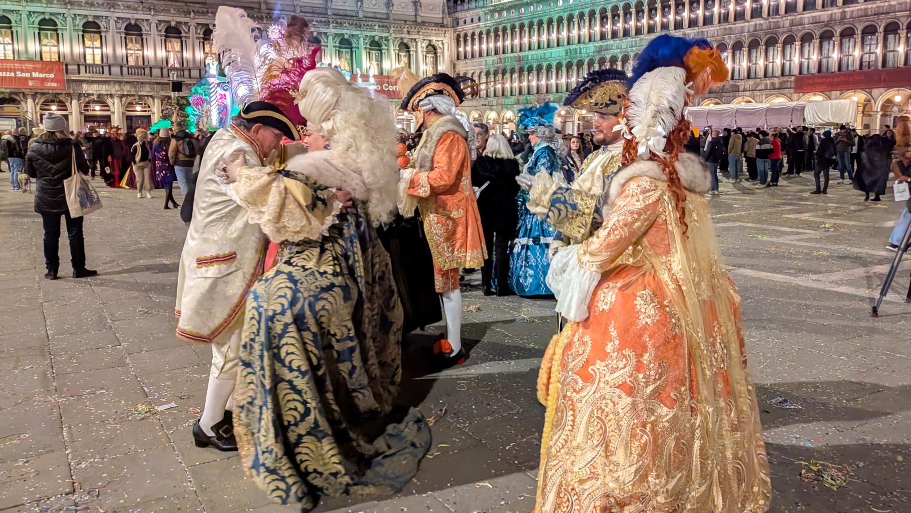 Účastníci karnevalu v Benátkach predvádzajú svoje dobové kostýmy na námestí Piazza San Marco počas
            večerného programu.
        